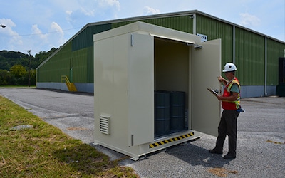 Man in a hardhat and orange safety vest inspecting a U.S. Chemical Stroage building full of chemical containers