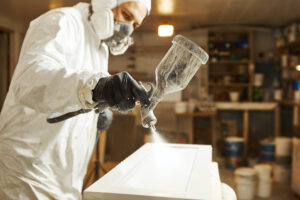 close-up of a person in a safety suit applying paint to a product, storage container for paint 
