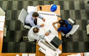 overhead view of two men and a woman seated around a table discussing chemical storage building plans, standards 