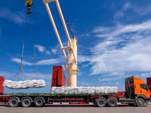 Sugar bags are loading in hold of bulk-vessel at industrial port crane picking up sugar bags from truck to load.