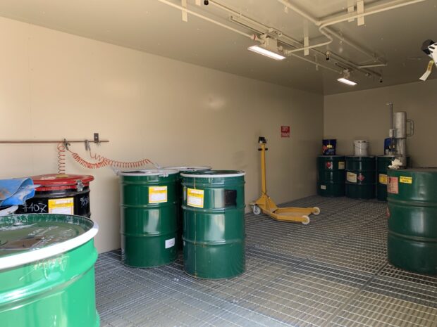 Interior photo of US Chemical Storage building for American Emergency Vehicles. Interior lighting illuminates 55 gallon drums with grounding buss bars as well as other equipment safe within. 