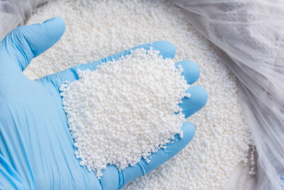 Closeup photo of a hand in blue glove holds white fertilizer for plants. Big bag with chemical NPK fertilizer for plants