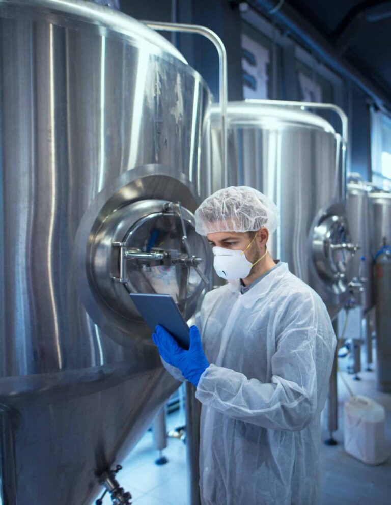 Factory worker technologist in protective uniform with hairnet and mask controlling food production on tablet computer.