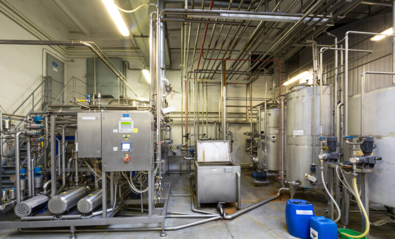 Lots of pipes and tanks in the shop of brewery in need of cleaning by appearances